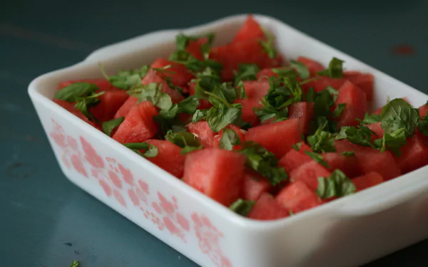 HD desktop wallpaper featuring a white dish filled with fresh watermelon cubes topped with chopped green herbs on a dark surface.