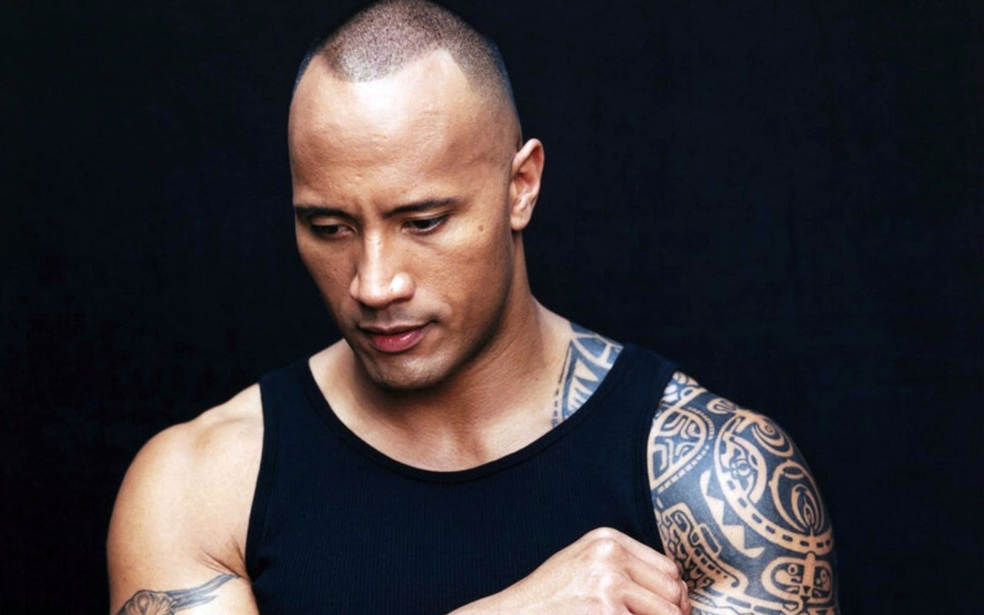 HD desktop wallpaper featuring celebrity Dwayne Johnson in a black tank top, showcasing his tattooed arm against a dark background.