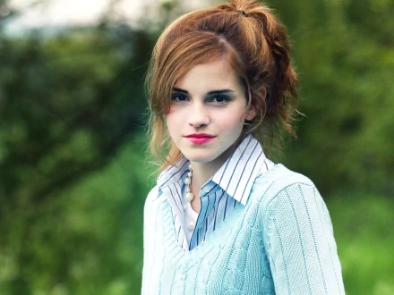 Emma Watson poses gracefully in a soft blue sweater, with a blurred green background, creating an inviting HD desktop wallpaper and background.