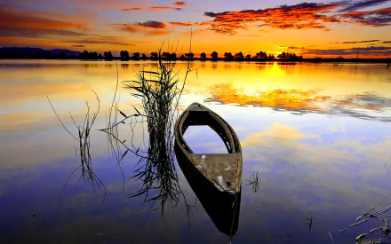 HD PC desktop wallpaper of a canoe floating calmly on a reflective lake at sunset, with vibrant orange and purple skies mirrored in the water.