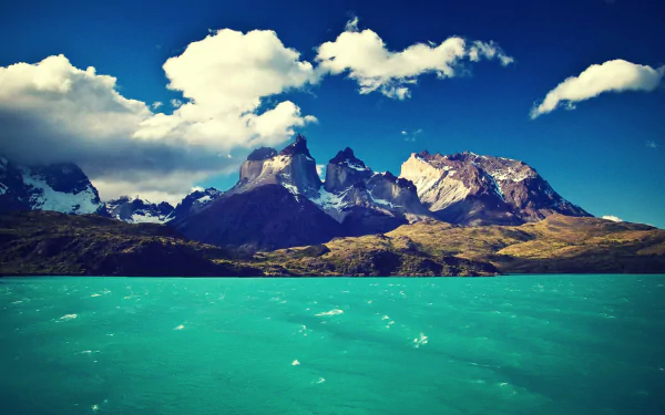 HD desktop wallpaper showcasing the striking turquoise waters and rugged peaks of Torres del Paine under a vibrant blue sky with scattered clouds.