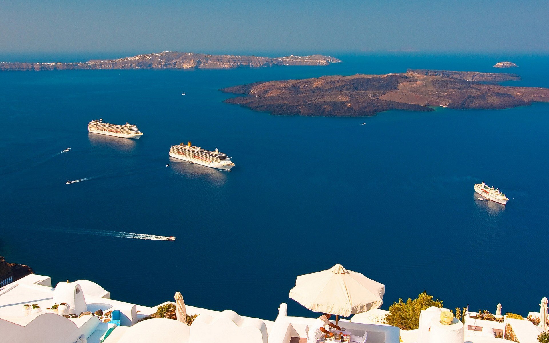 A stunning HD desktop wallpaper showcasing multiple cruise ships sailing on deep blue waters near rocky islands, viewed from a white terrace overlooking the sea.