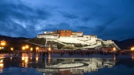 HD PC desktop wallpaper of the man-made Potala Palace at dusk, its illuminated white and red complex reflected on a wet plaza under a deep blue sky.