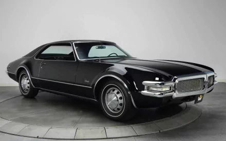 HD desktop wallpaper featuring a sleek black 1968 Oldsmobile Toronado against a plain gray background.