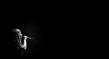 Black-and-white HD PC desktop wallpaper of a reggae singer with dreadlocks singing into a microphone against a dark, empty background.