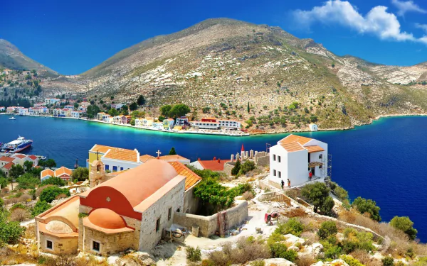 HD PC desktop wallpaper/background of Kastelorizo's man-made harbor and whitewashed buildings on a rocky shore, vivid blue sea and sunlit hillside.