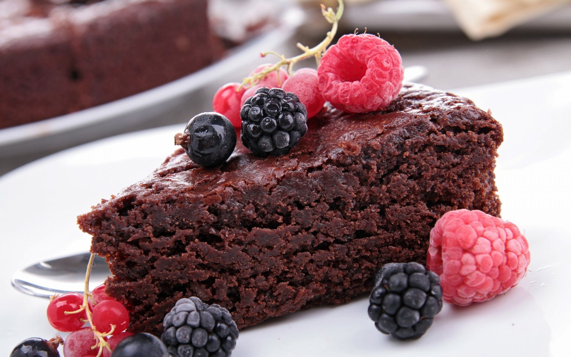 HD desktop wallpaper featuring a close-up of a slice of rich chocolate cake garnished with fresh raspberries, blackberries, and red currants, set on a white plate.