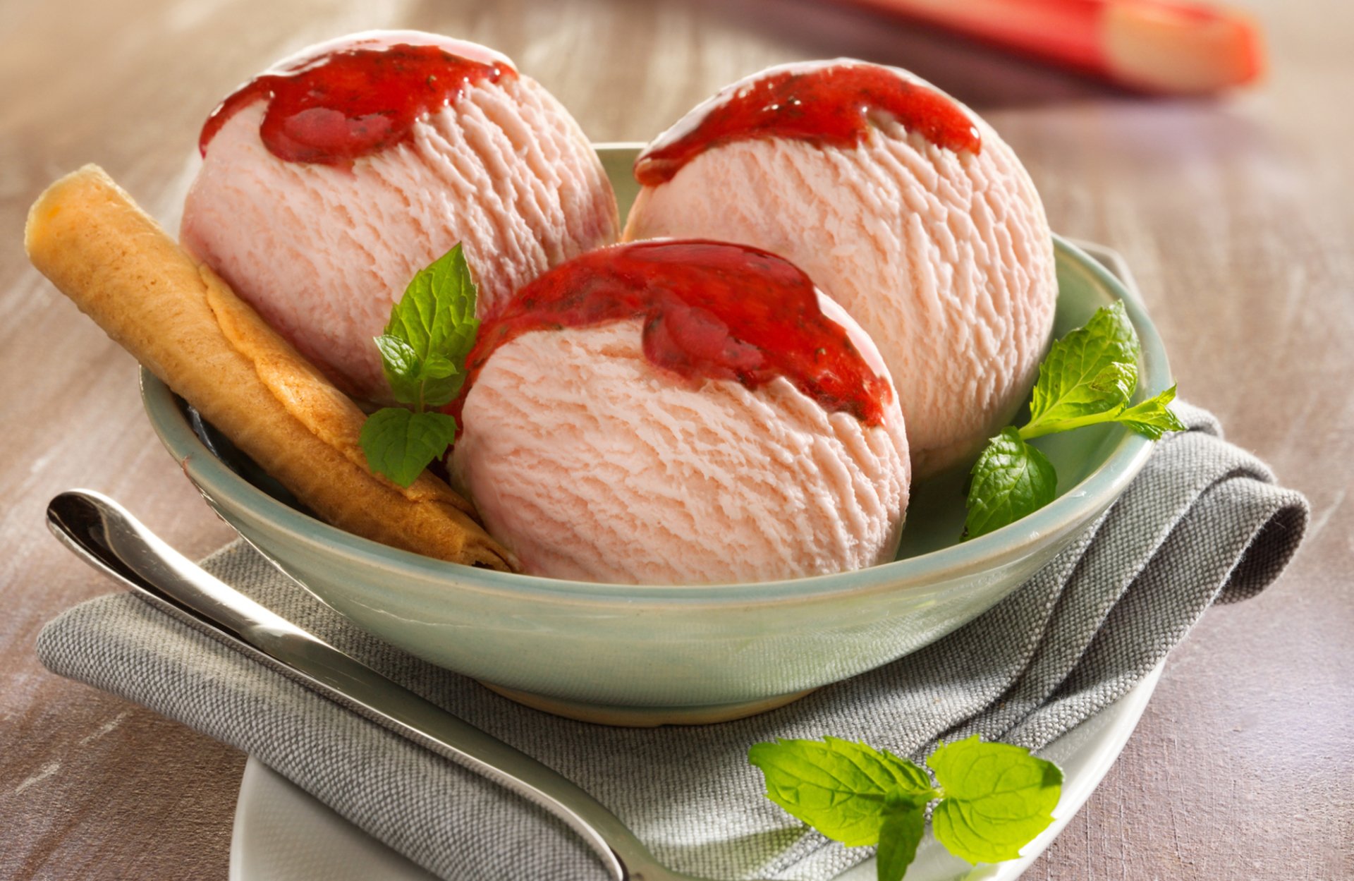 HD desktop wallpaper featuring a bowl of strawberry ice cream topped with syrup, garnished with mint leaves and a cookie, set on a wooden table.
