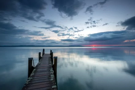 HD desktop wallpaper featuring a man-made wooden pier extending into calm water under a cloudy sky at sunset.