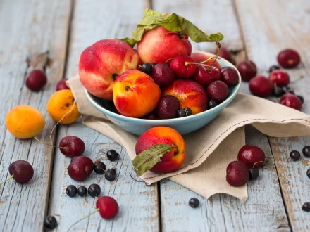 A vibrant bowl of peaches, cherries, and apricots sits on a rustic wooden table, surrounded by scattered fruits. This high-definition image serves as a colorful desktop wallpaper.