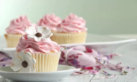 HD wallpaper featuring a row of cupcakes with pink frosting and white flower decorations, presented on a softly lit table with a floral fabric.
