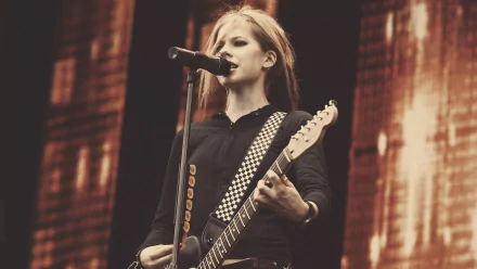 Avril Lavigne performing on stage, showcasing her energy and style while playing guitar. An HD desktop wallpaper capturing the essence of music and rock culture.