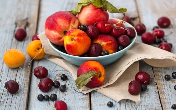 A vibrant bowl of peaches, cherries, and apricots sits on a rustic wooden table, surrounded by scattered fruits. This high-definition image serves as a colorful desktop wallpaper.