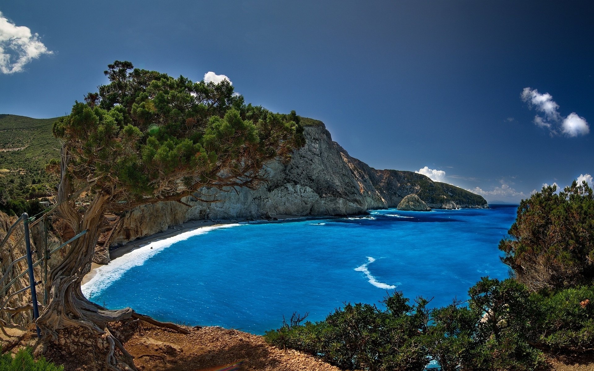 HD PC desktop wallpaper featuring a vibrant coastline with clear blue waters, rocky cliffs, and lush greenery under a bright blue sky.