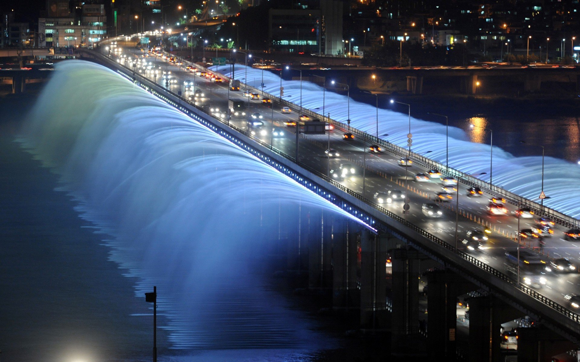 HD PC desktop wallpaper of Banpo Bridge — a man-made night scene with blue-lit waterfall curtains spilling into the river, framed by city lights and moving traffic.