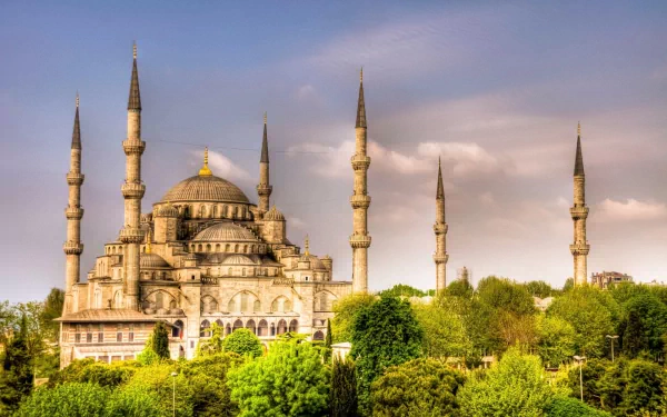 Religious HD PC desktop wallpaper featuring the Sultan Ahmed Mosque with its domes and six minarets rising above green trees beneath a pastel sky.