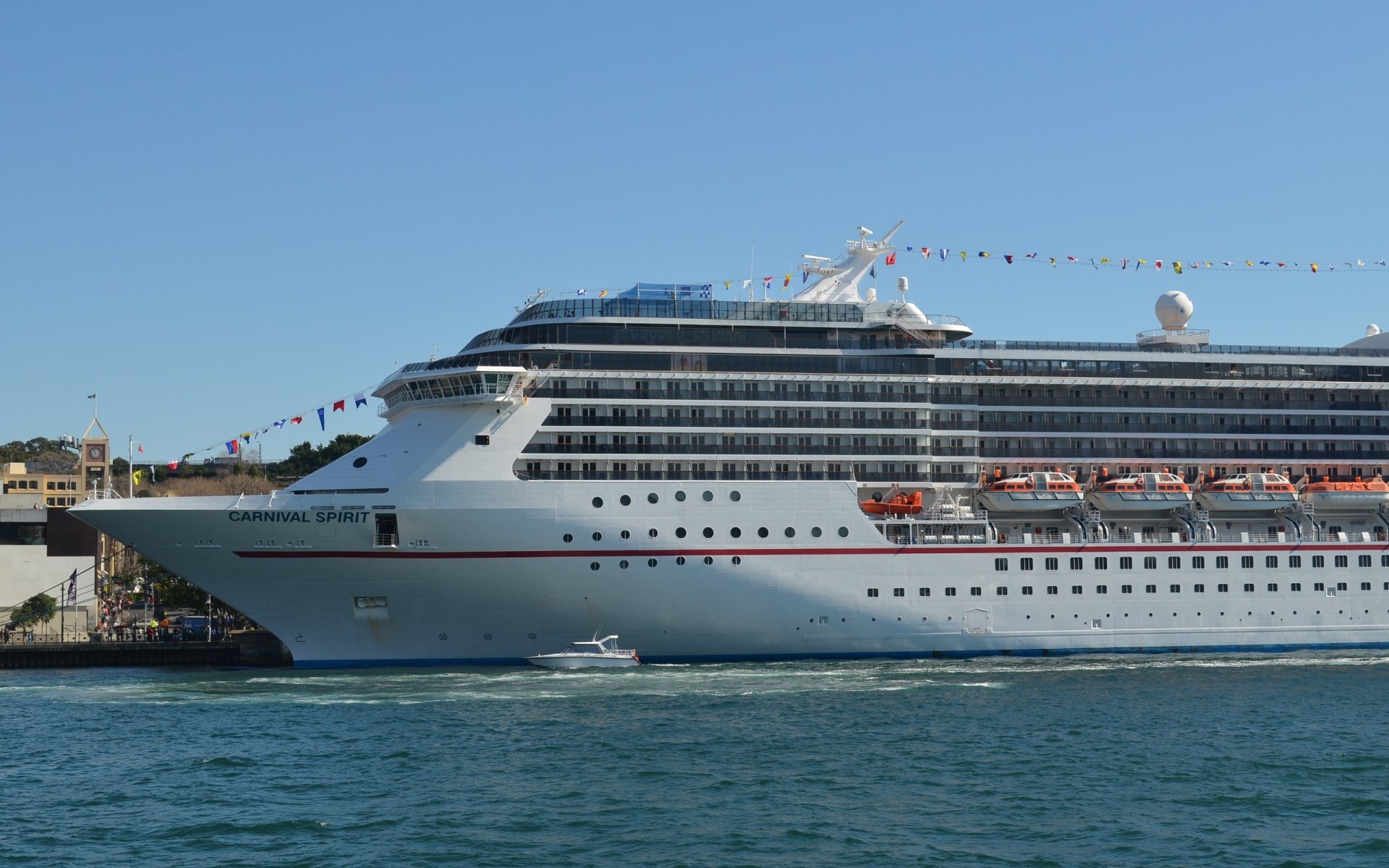 Panoramic 2K Quad HD PC desktop wallpaper: Carnival Spirit cruise ship (vehicle) docked in Sydney harbor, white passenger ship and small boat on blue water under clear sky.