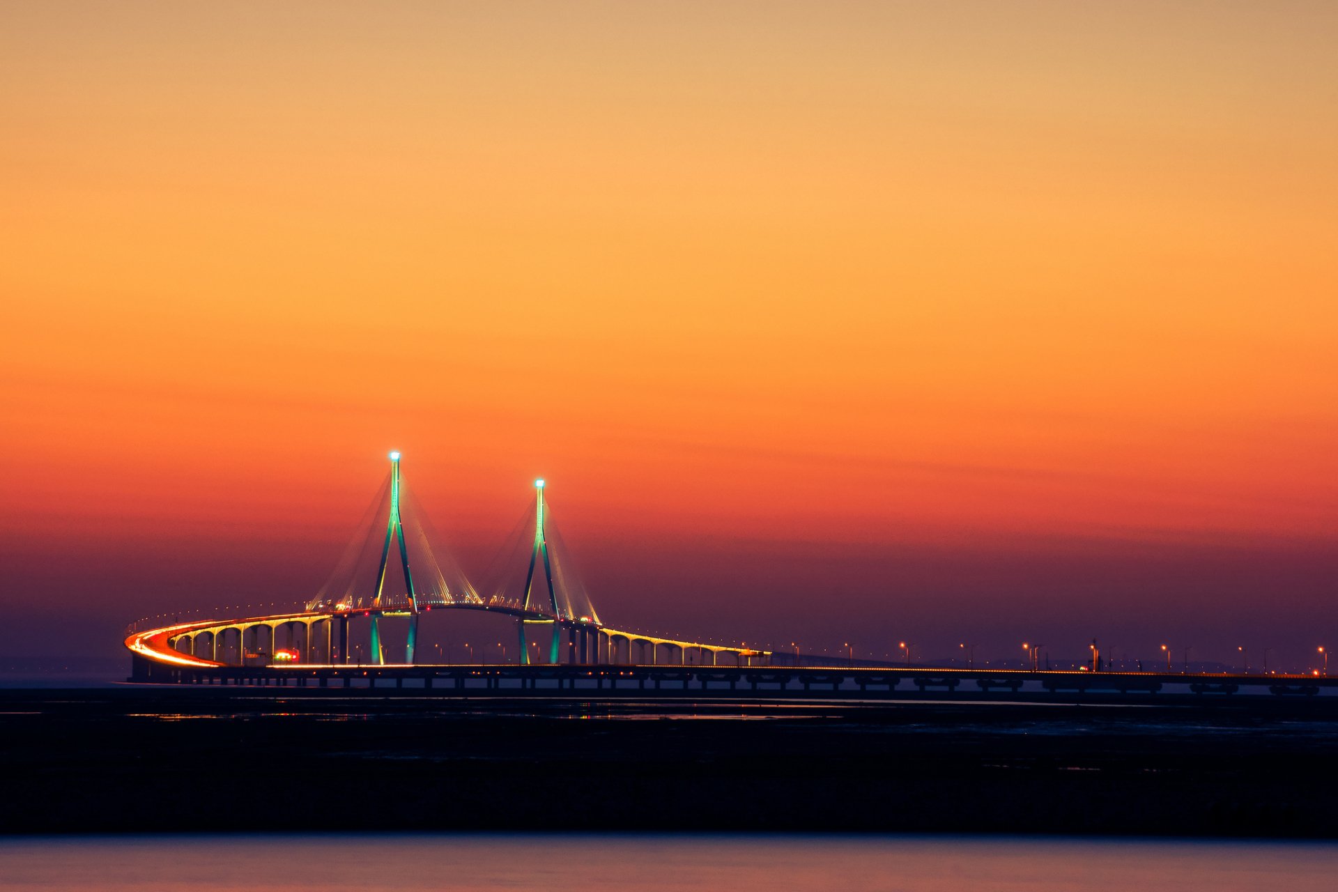 HD desktop wallpaper showing the man-made Incheon Bridge illuminated against a vibrant orange sunset sky.