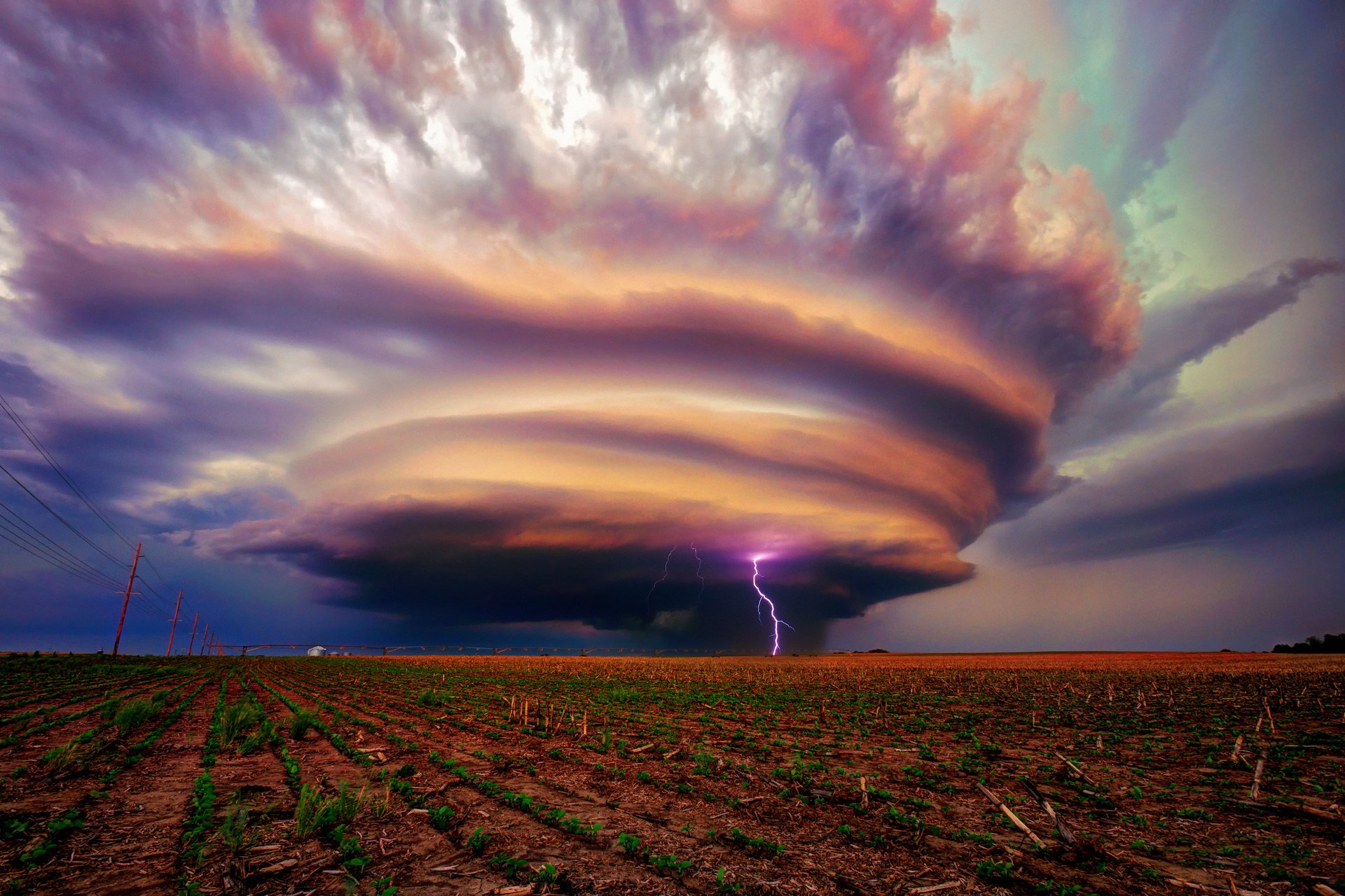 HD desktop wallpaper of a dramatic landscape featuring a massive, swirling storm cloud with a striking bolt of lightning, set against a dusk sky.