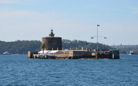 Fort Denison, a man-made island with a stone fort and building in Sydney Harbour, Australia, set against blue water and a clear sky.