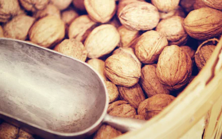 HD desktop wallpaper showing a close-up of whole walnuts in a basket with a metal scoop, highlighting natural textures and warm tones.