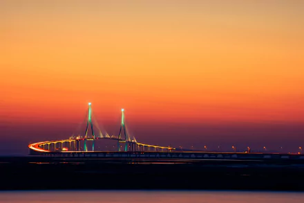 HD desktop wallpaper showing the man-made Incheon Bridge illuminated against a vibrant orange sunset sky.