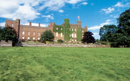 2K Quad HD desktop wallpaper of Scone Palace: ivy-covered stone manor with flag, set beyond a sweeping green lawn and trees under a bright blue sky (man-made)