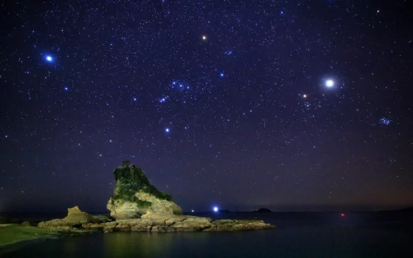 A stunning HD wallpaper featuring the Orion constellation shining brightly in a night sky above a serene coastal landscape. The stars illuminate the tranquil waters, creating a captivating natural scene.