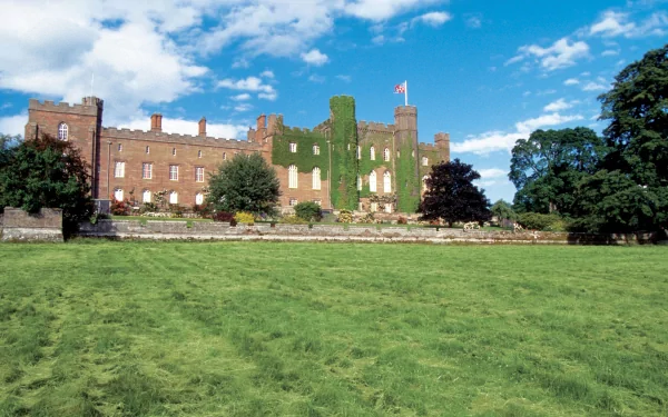2K Quad HD desktop wallpaper of Scone Palace: ivy-covered stone manor with flag, set beyond a sweeping green lawn and trees under a bright blue sky (man-made)