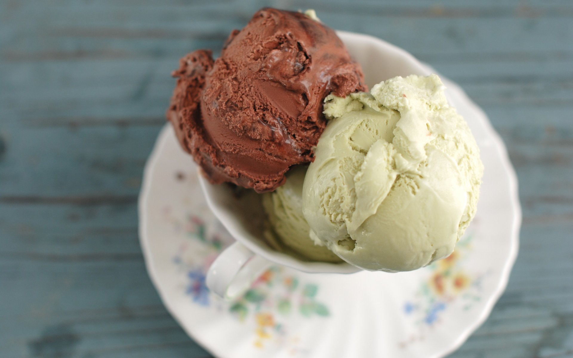 HD PC desktop wallpaper featuring two scoops of chocolate and vanilla ice cream in a white cup on a floral saucer against a blue wooden background.