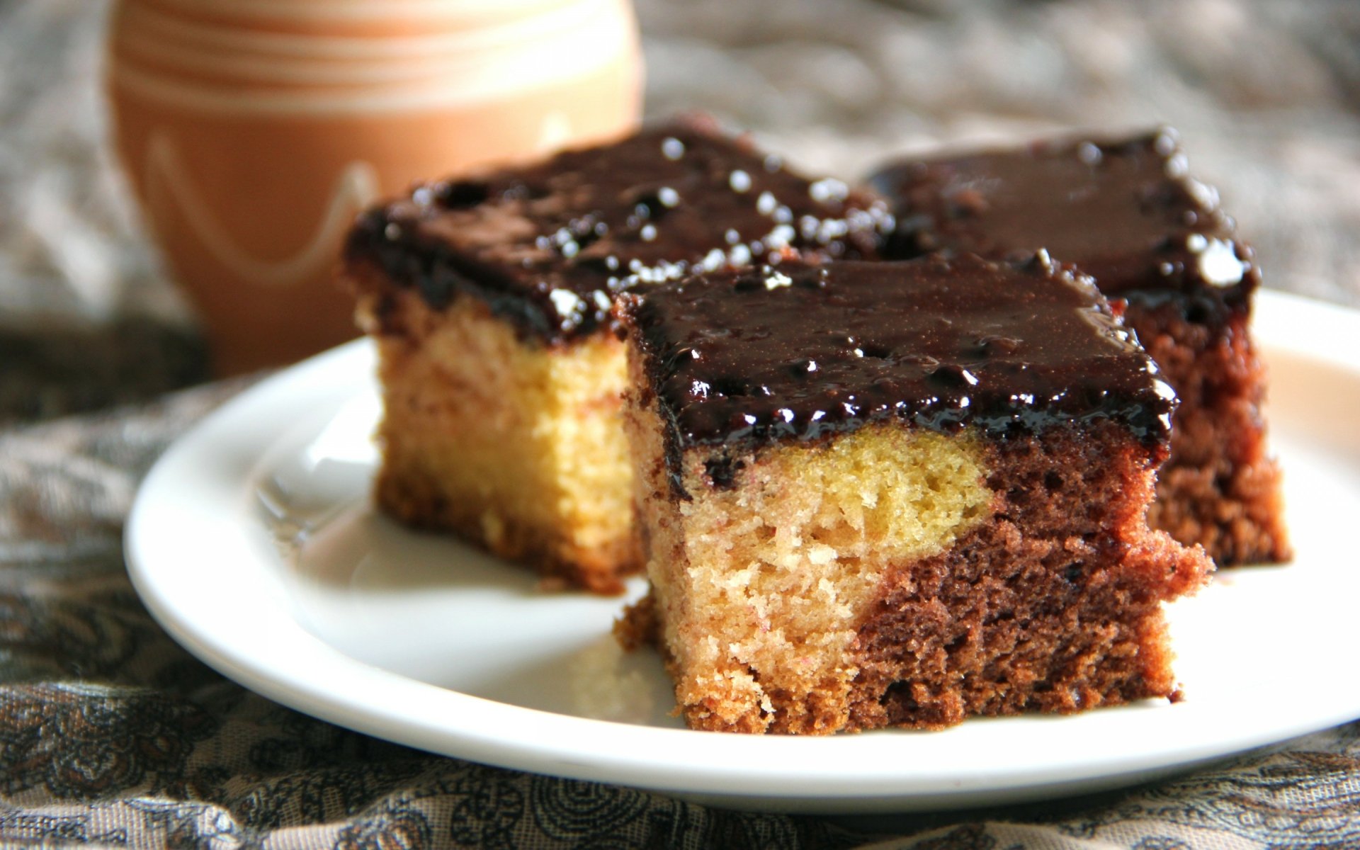 HD PC desktop wallpaper featuring a close-up of three chocolate-glazed layered cake squares on a white plate with a blurred background.