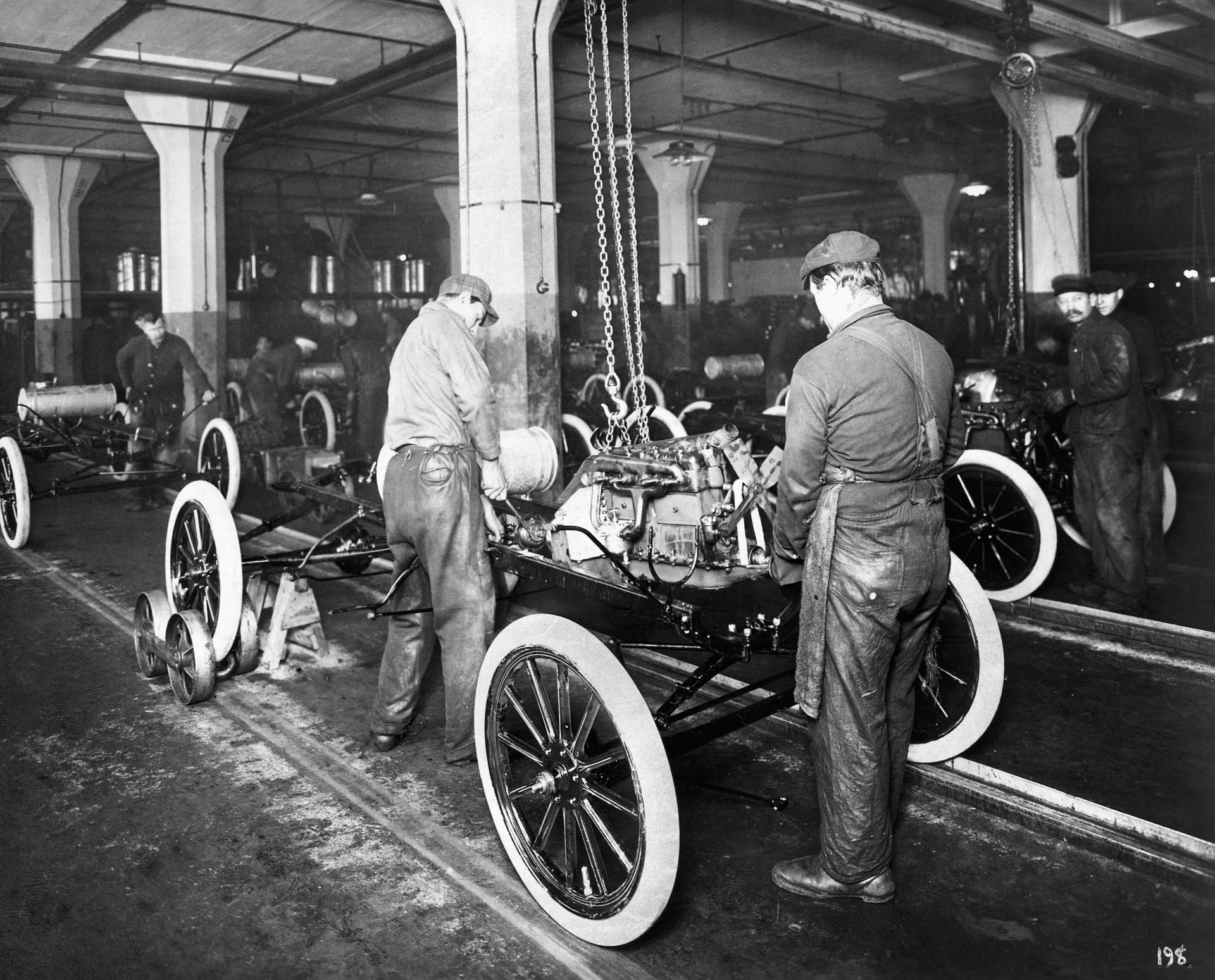 Black-and-white HD desktop wallpaper showing workers assembling a Ford Model T vehicle inside a factory.