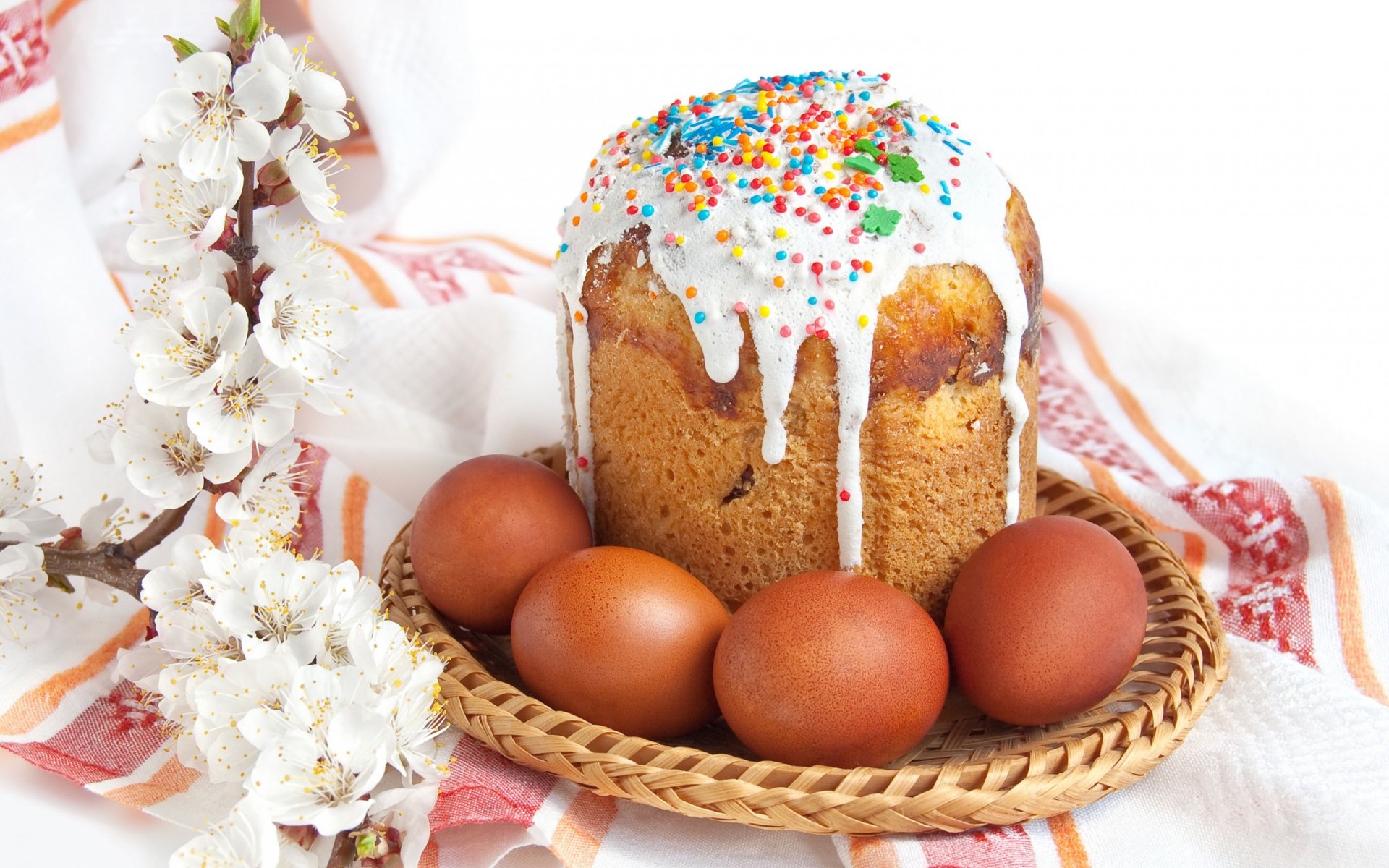 HD PC desktop wallpaper showing a traditional Easter cake with white icing and colorful sprinkles, surrounded by brown eggs and white blossoms, celebrating the holiday.