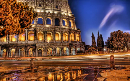HD desktop wallpaper showcasing the illuminated man-made Colosseum at night with light trails and reflections on the wet pavement.