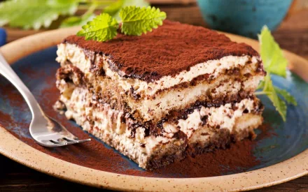 A rich chocolate cake layered with creamy filling and dusted with cocoa, served on a rustic plate, making an enticing HD desktop wallpaper for food lovers.