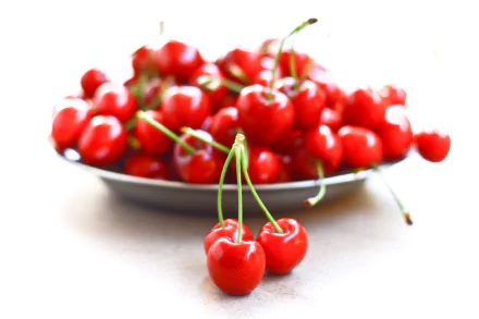 HD desktop wallpaper featuring a close-up of fresh, vibrant red cherries on a plate with a few cherries in the foreground against a bright white background.