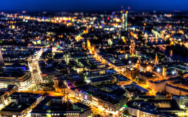 HD desktop wallpaper of Frankfurt, Germany — aerial nighttime view of a man-made cityscape with glowing streets, lit skyscrapers and river reflections.
