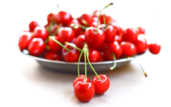 HD desktop wallpaper featuring a close-up of fresh, vibrant red cherries on a plate with a few cherries in the foreground against a bright white background.