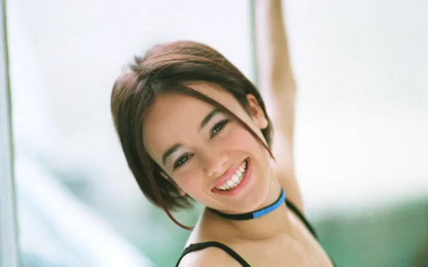HD PC desktop wallpaper featuring a smiling Alizée, capturing a bright and joyful moment in a soft, natural setting with a light, blurred background.