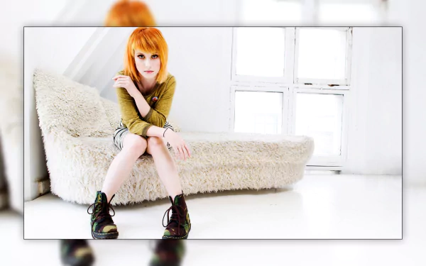 HD PC desktop wallpaper featuring Hayley Williams seated in a bright, minimalist room, emphasizing her vibrant hair and distinctive style in a music-themed image.