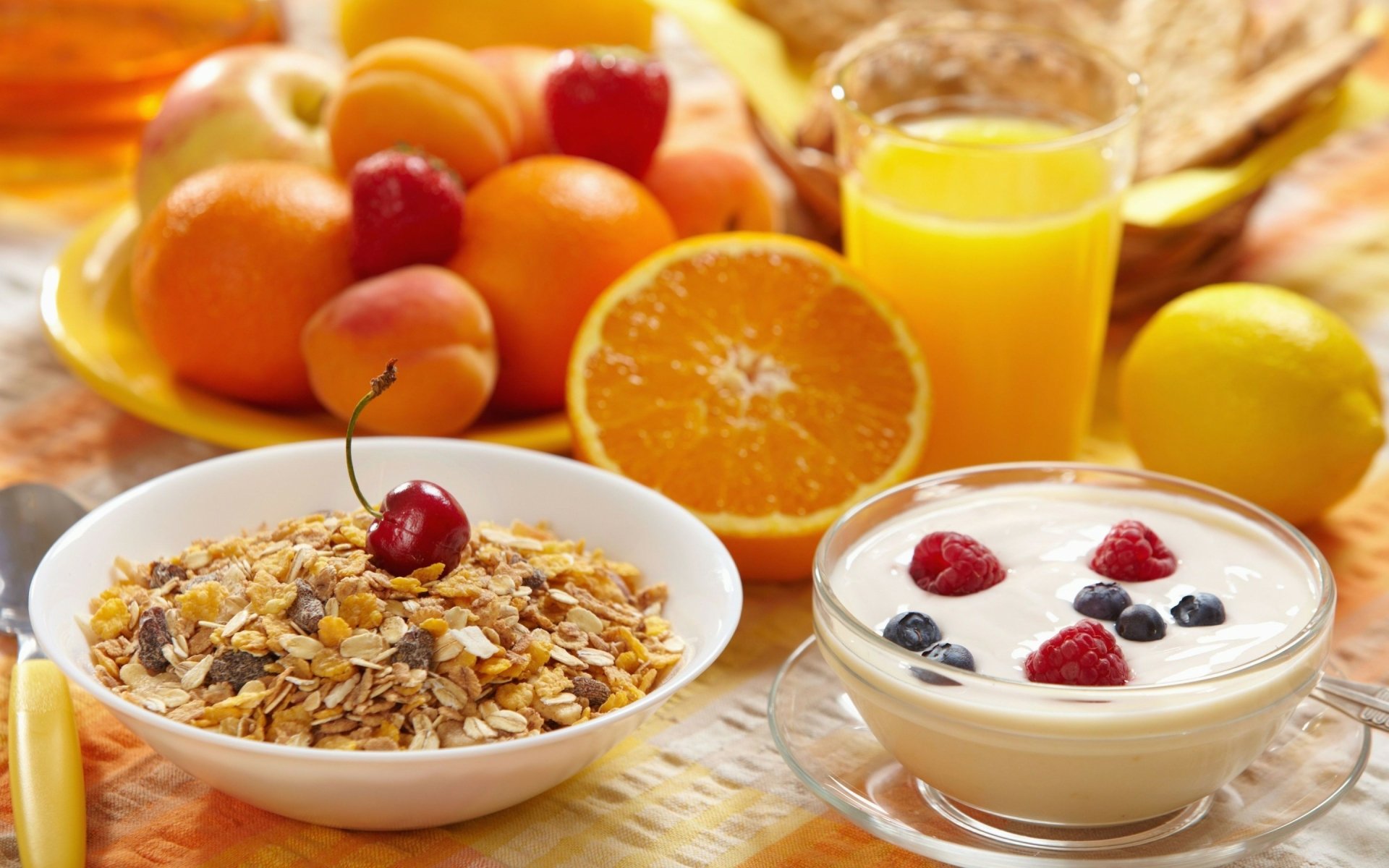 A vibrant breakfast scene featuring a bowl of oatmeal topped with a cherry, yogurt with blueberries and raspberries, fresh oranges, and a glass of orange juice, set against a bright background.
