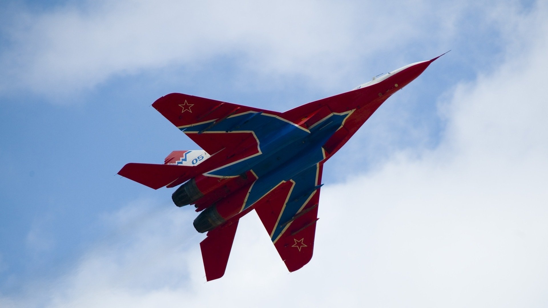 HD desktop wallpaper featuring a vibrant red and blue military jet performing a maneuver at an air show against a cloudy sky backdrop.