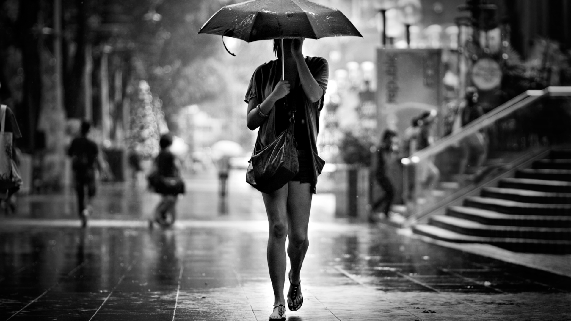 Black-and-white HD desktop wallpaper featuring a woman model walking barefoot on a rainy city street, holding an umbrella.