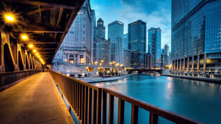 A serene view of Chicago’s skyline at dusk, featuring illuminated buildings and a tranquil river, captured from a wooden walkway along the water. Suitable as a HD desktop wallpaper.