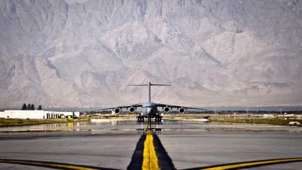 A Boeing C-17 Globemaster III stands on a runway, flanked by mountains, set against a clear sky, showcasing its impressive military design and stature.