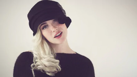 HD desktop wallpaper featuring a woman with blonde hair wearing a black cap, looking stylish in a soft, beige-toned background.