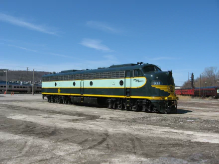 HD PC desktop wallpaper background of a teal-and-yellow diesel locomotive train vehicle parked in a rail yard under a clear blue sky.