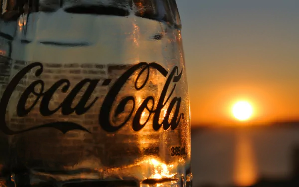 Close-up of a Coca-Cola bottle reflecting the warm glow of a sunset, captured in an HD man-made desktop wallpaper background.