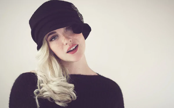 HD desktop wallpaper featuring a woman with blonde hair wearing a black cap, looking stylish in a soft, beige-toned background.