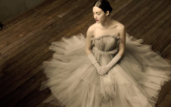HD desktop wallpaper featuring celebrity Emmy Rossum in an elegant, flowing gown seated gracefully on a wooden floor.